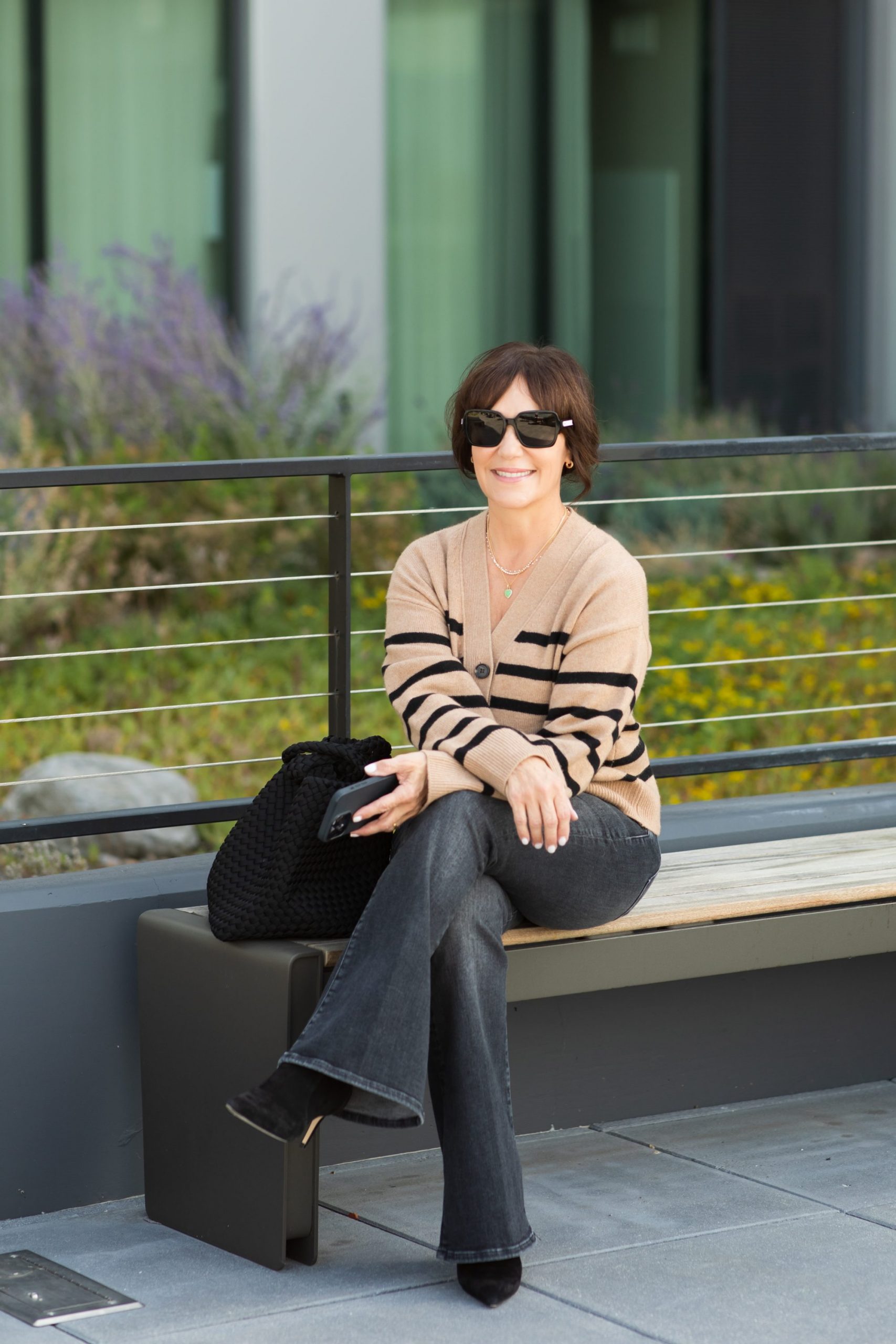 Susie wearing casual fall outfit with tan and black stripe sweater, grey flare jeans, and black boots. 