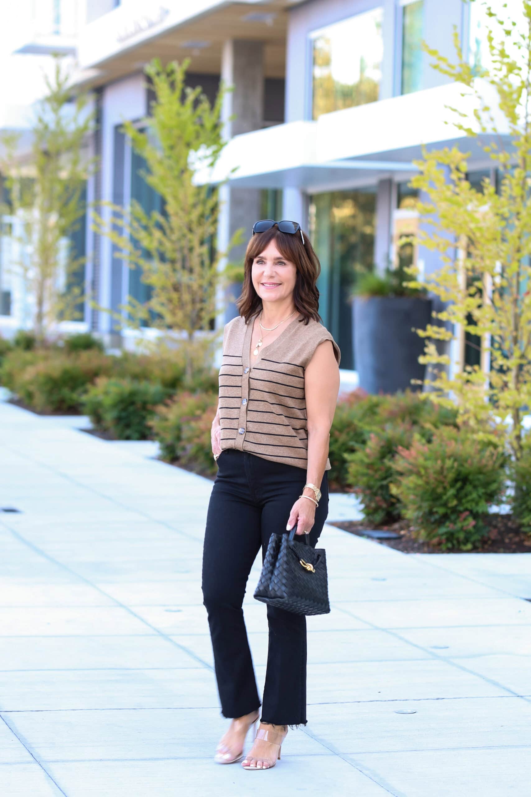 Susie wearing casual sunny fall outfit with brown sweater vest, black jeans, and black back.