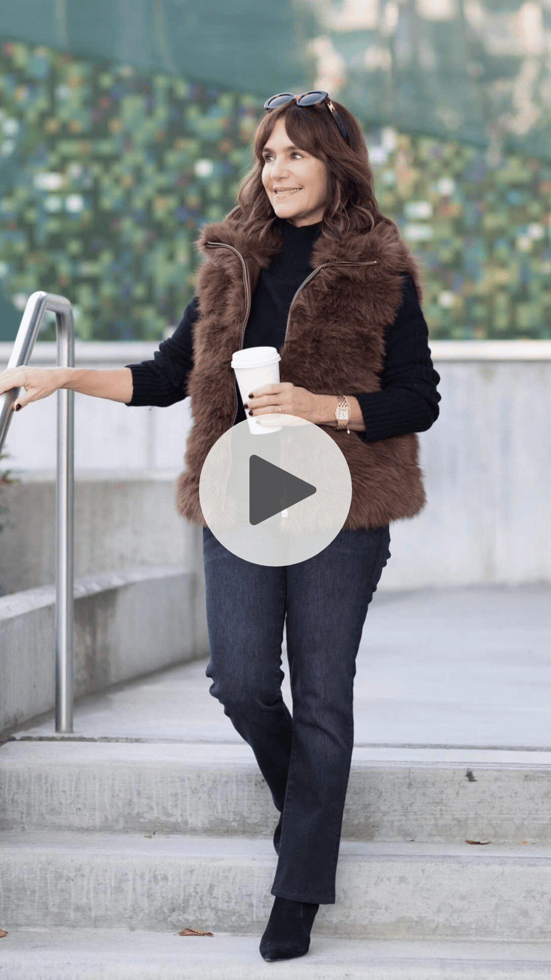 Susie wearing a cozy casual fall outfit with brown faux fur vest, black sweater, grey jeans and black suede boots.