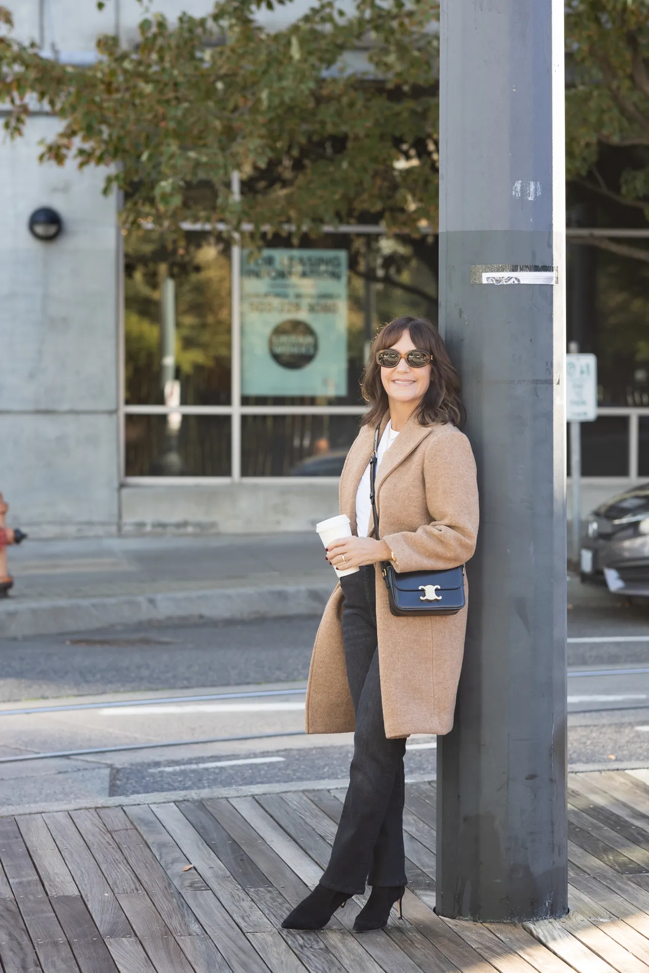 Susie wearing casual fall outfit with camel wool coat, grey jeans, and black boots.