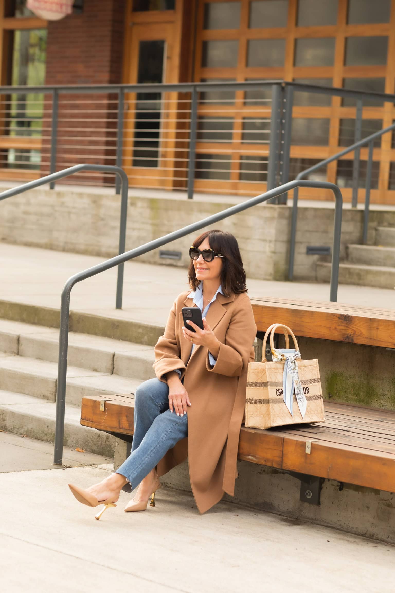 Susie sitting wearing camel colored wool wrap coat and slim straight jeans for casual, everyday outfit.