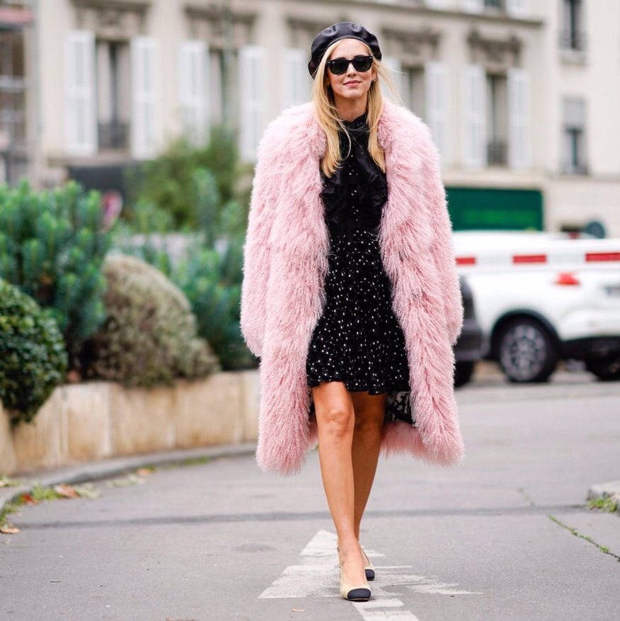Woman wearing pink fur knee length coat over a black dress with sunglasses and a leather beret