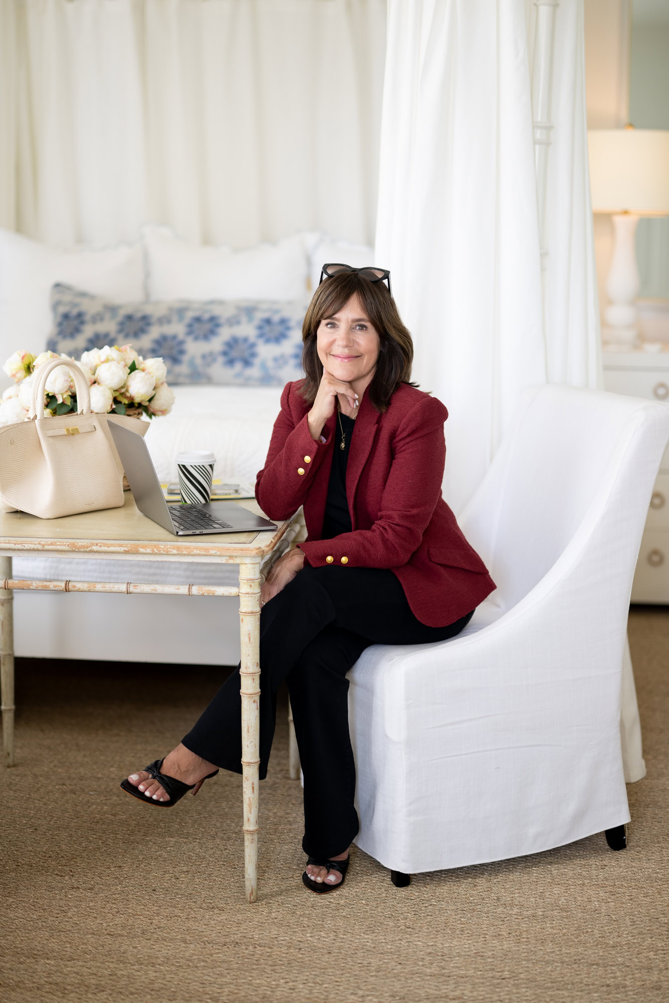 Susie sitting at table wearing burgundy blazer with gold buttons, black flare jeans and black open toe sandals
